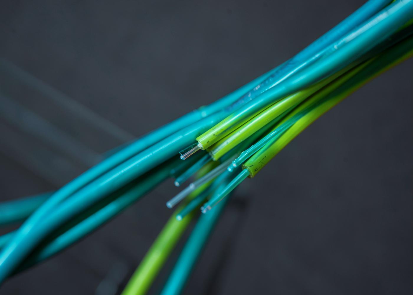 Bundle of green and teal fibre optic cables against a dark surface
